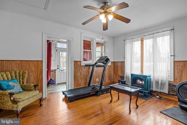 workout room featuring ceiling fan, wooden walls, wood-type flooring, and a wood stove