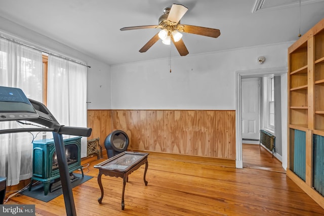 workout area with light wood-type flooring, wooden walls, ceiling fan, and a wood stove