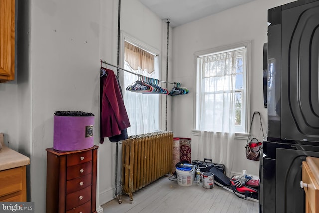 interior space featuring stacked washer and dryer, radiator, and light hardwood / wood-style flooring