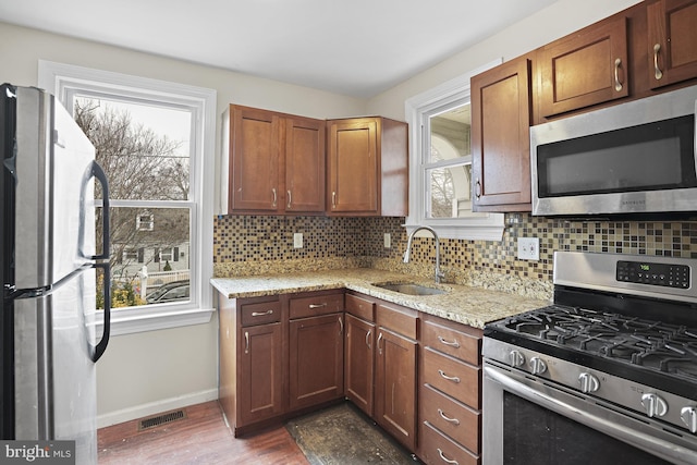 kitchen with sink, appliances with stainless steel finishes, light stone counters, dark hardwood / wood-style flooring, and decorative backsplash