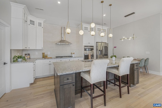 kitchen featuring white cabinetry, stainless steel appliances, light hardwood / wood-style floors, a center island with sink, and decorative light fixtures