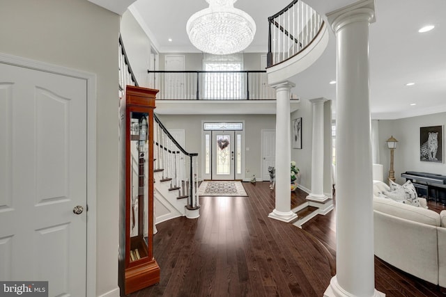 entrance foyer featuring stairway, ornamental molding, wood finished floors, an inviting chandelier, and ornate columns