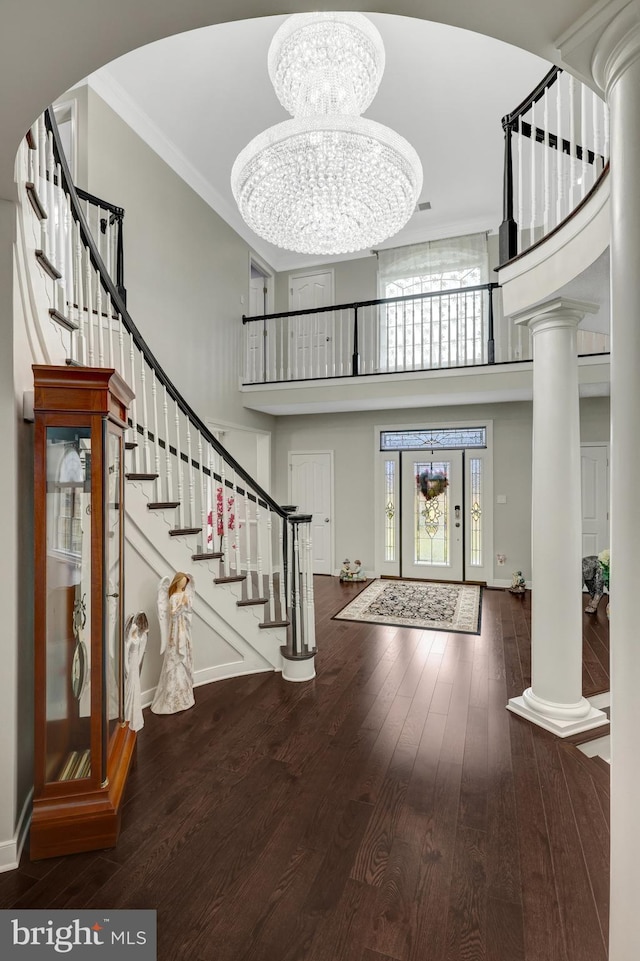 foyer featuring a notable chandelier, wood finished floors, a towering ceiling, and ornate columns