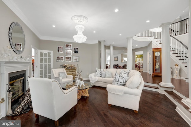 living room featuring decorative columns, dark wood finished floors, a glass covered fireplace, stairs, and crown molding