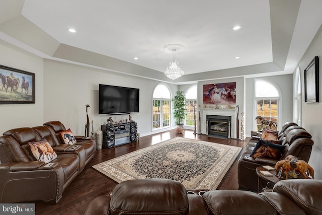 living area with a raised ceiling, wood finished floors, an inviting chandelier, a fireplace, and recessed lighting