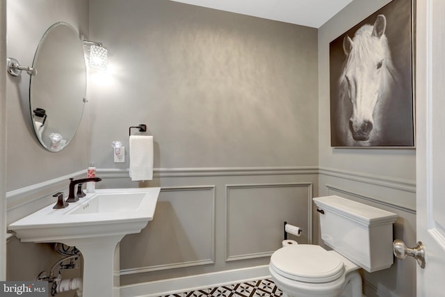 half bath with a wainscoted wall, a decorative wall, and toilet