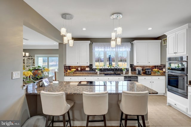 kitchen featuring stainless steel appliances, backsplash, white cabinets, a sink, and a kitchen bar