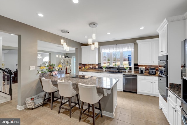 kitchen with white cabinets, decorative backsplash, a breakfast bar area, dark stone countertops, and black appliances