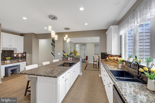 kitchen with white cabinets, dishwasher, a breakfast bar area, black electric cooktop, and a sink