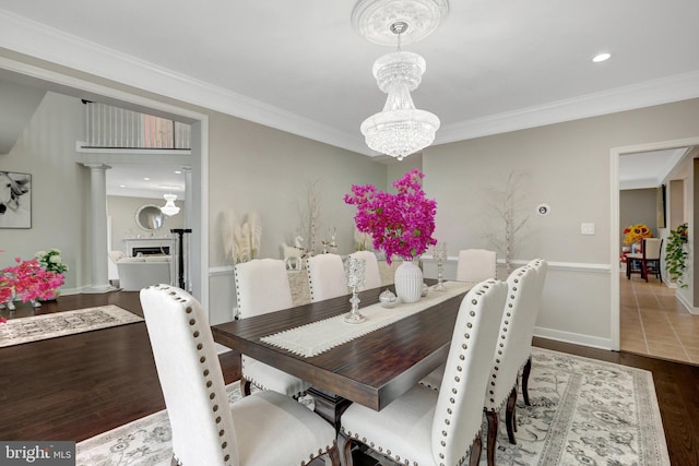 dining space with crown molding, a fireplace, a chandelier, and wood finished floors