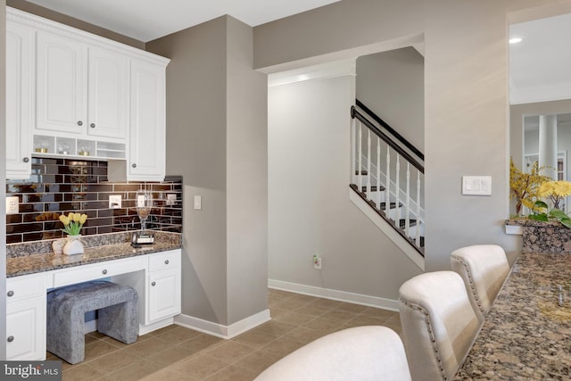 kitchen featuring light tile patterned flooring, white cabinetry, baseboards, tasteful backsplash, and dark stone countertops