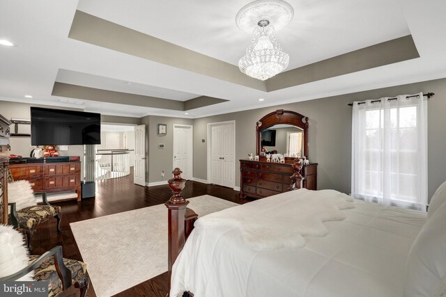 bedroom with a chandelier, a raised ceiling, dark wood finished floors, and baseboards