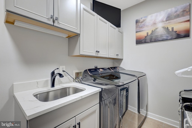 clothes washing area with cabinet space, light tile patterned floors, baseboards, washer and dryer, and a sink