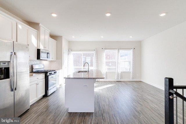 kitchen featuring sink, white cabinetry, stainless steel appliances, light stone counters, and a center island with sink