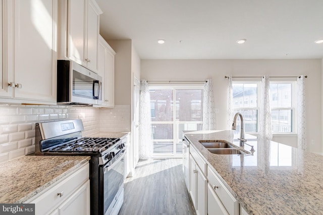 kitchen with sink, backsplash, white cabinets, light stone counters, and stainless steel appliances