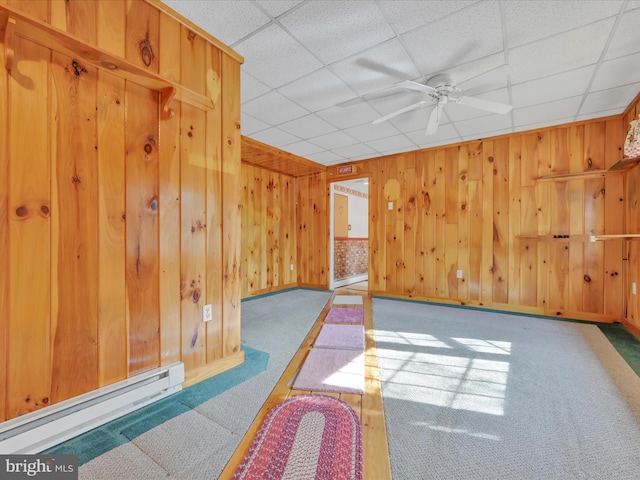 spare room with ceiling fan, wooden walls, a paneled ceiling, and a baseboard heating unit