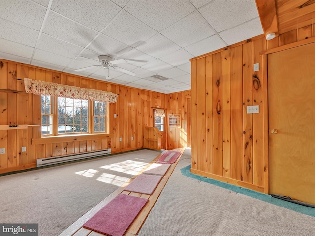 unfurnished living room featuring carpet floors, a baseboard radiator, wooden walls, and ceiling fan