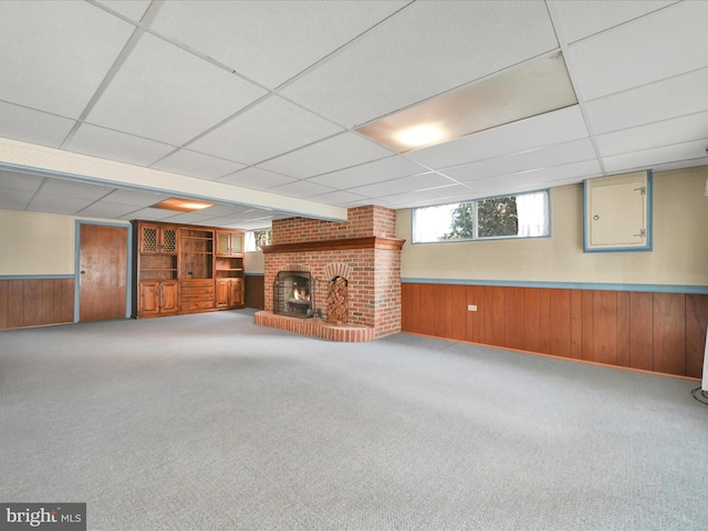 basement with carpet floors, a fireplace, a drop ceiling, and wood walls