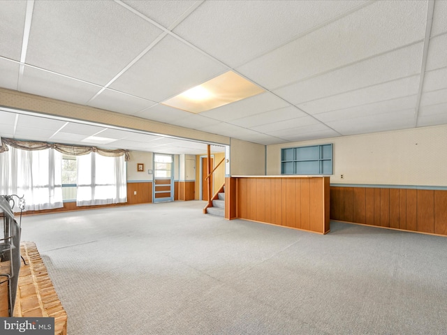 unfurnished room featuring carpet flooring, a paneled ceiling, and wooden walls