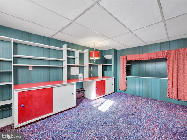 unfurnished office featuring a paneled ceiling, carpet flooring, built in desk, and wood walls