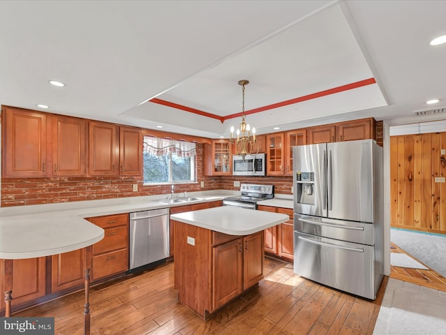 kitchen with stainless steel appliances, a raised ceiling, a center island, and decorative light fixtures