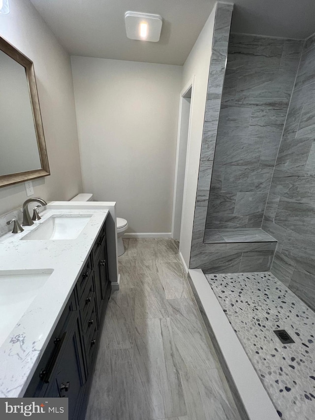 bathroom featuring vanity, a tile shower, and toilet