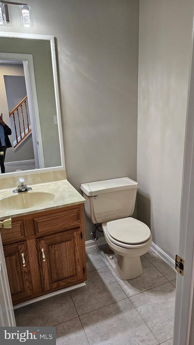 half bath featuring tile patterned flooring, toilet, vanity, and baseboards