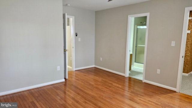 unfurnished bedroom featuring ensuite bath, light wood-type flooring, and baseboards