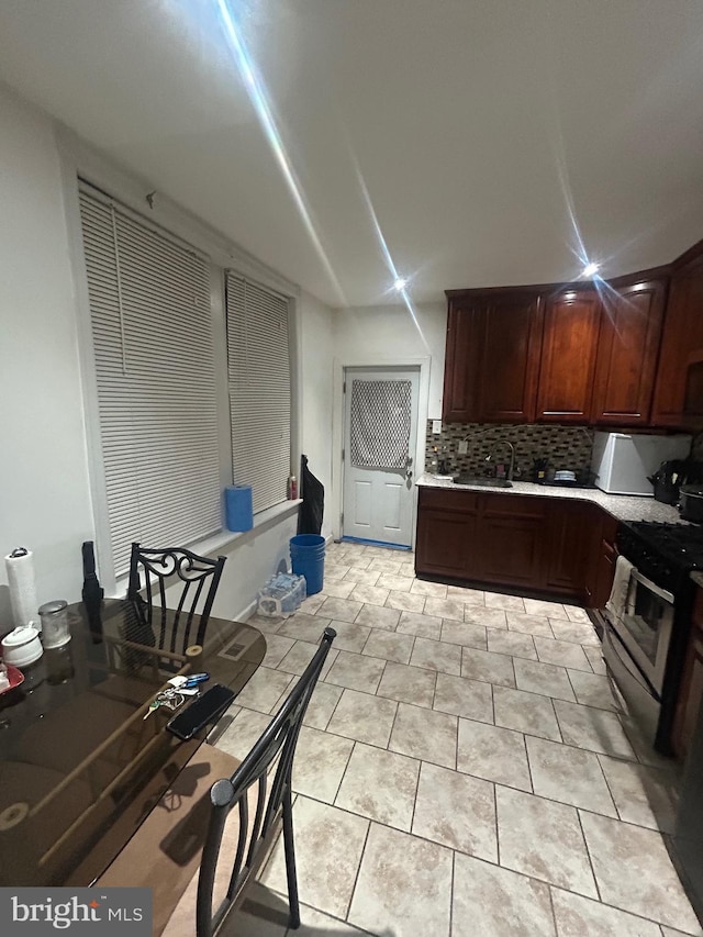 kitchen with tasteful backsplash, sink, light tile patterned floors, and stainless steel gas range oven