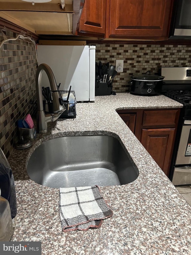 kitchen with appliances with stainless steel finishes, sink, backsplash, and light stone counters