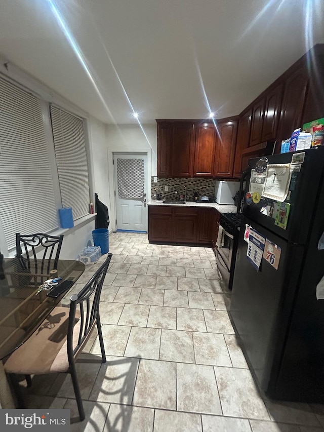 kitchen with tasteful backsplash, gas range, black fridge, and light tile patterned flooring