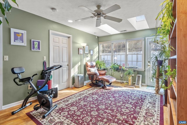 workout room with ceiling fan, a skylight, a textured ceiling, and light wood-type flooring