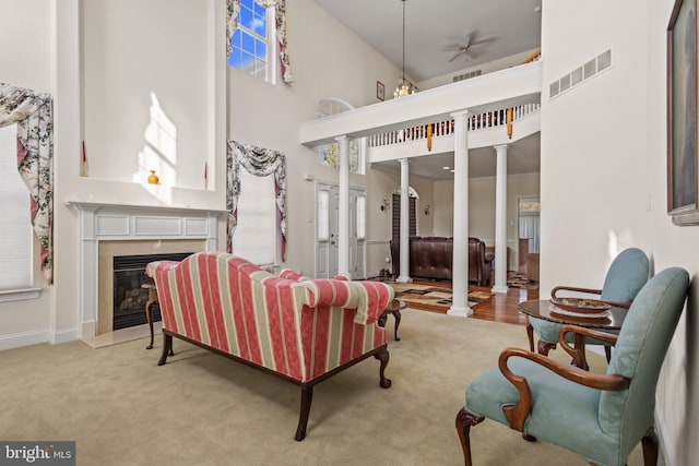 carpeted living room featuring a fireplace, ornate columns, and a towering ceiling