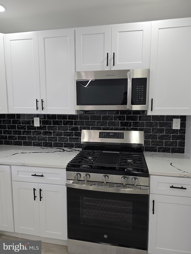 kitchen with decorative backsplash, light stone countertops, white cabinets, and appliances with stainless steel finishes