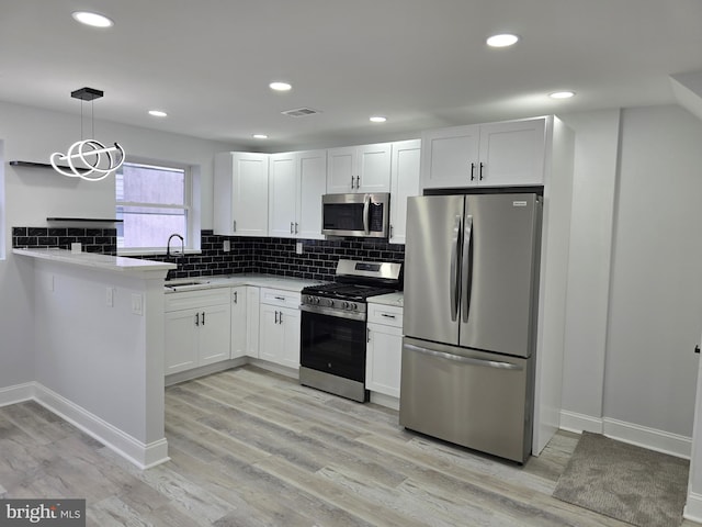 kitchen featuring stainless steel appliances, tasteful backsplash, light hardwood / wood-style floors, white cabinets, and decorative light fixtures