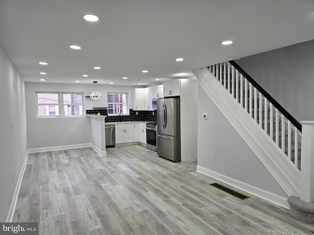 kitchen featuring sink, white cabinetry, light hardwood / wood-style flooring, appliances with stainless steel finishes, and pendant lighting