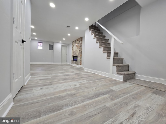 basement with a stone fireplace and light hardwood / wood-style flooring