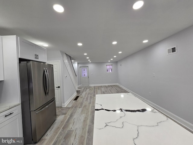 kitchen featuring white cabinetry, light stone countertops, stainless steel fridge, and light hardwood / wood-style floors