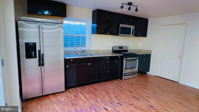 kitchen with stainless steel appliances, sink, light stone counters, and light wood-type flooring