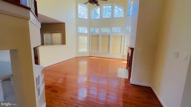 unfurnished living room featuring hardwood / wood-style flooring, ceiling fan, and a high ceiling