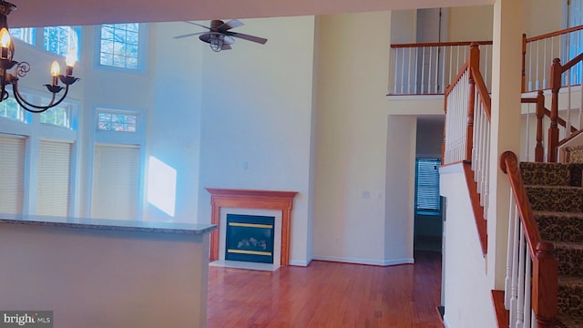 unfurnished living room with a towering ceiling, ceiling fan with notable chandelier, and light hardwood / wood-style floors