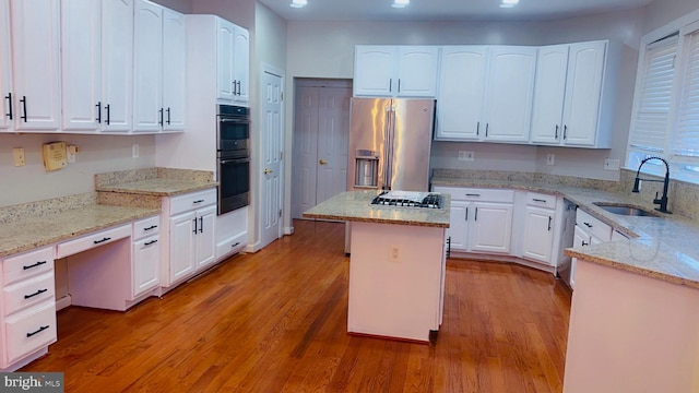 kitchen with sink, appliances with stainless steel finishes, light stone counters, white cabinets, and a kitchen island