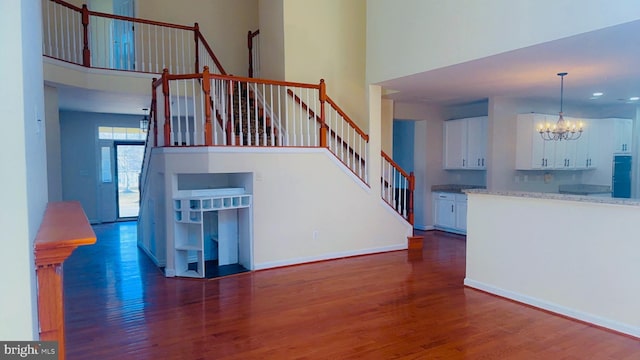 stairs with an inviting chandelier, a towering ceiling, and wood-type flooring