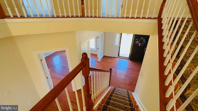 stairway with wood-type flooring and a towering ceiling