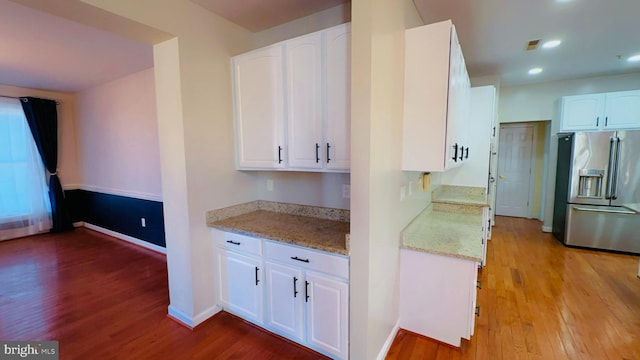 kitchen featuring light stone countertops, high quality fridge, white cabinets, and light hardwood / wood-style flooring