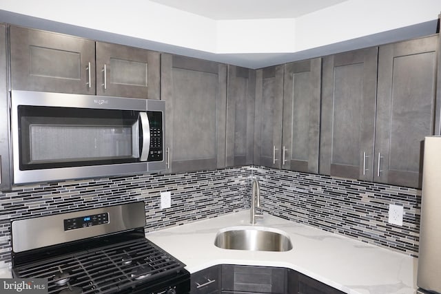 kitchen featuring sink, backsplash, stainless steel appliances, light stone countertops, and dark brown cabinets