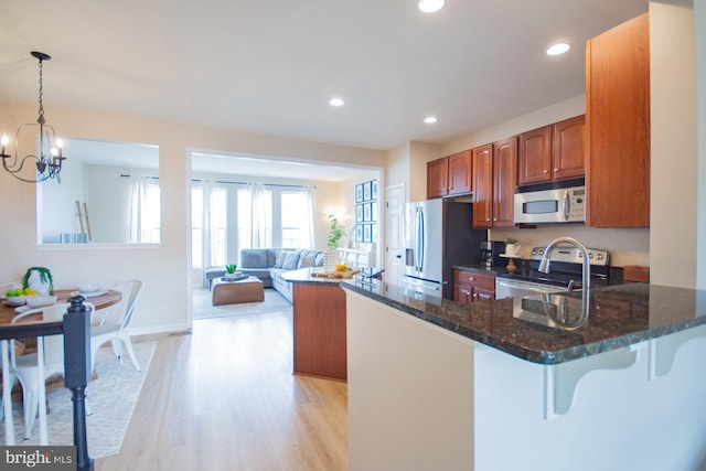 kitchen with pendant lighting, dark stone countertops, light hardwood / wood-style floors, kitchen peninsula, and stainless steel appliances