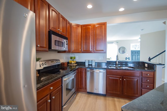 kitchen with dark stone countertops, sink, light wood-type flooring, and appliances with stainless steel finishes