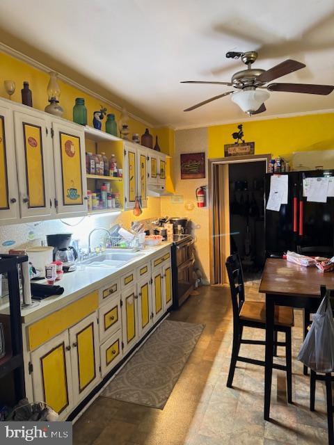 kitchen featuring sink, ceiling fan, black refrigerator, ornamental molding, and range with two ovens