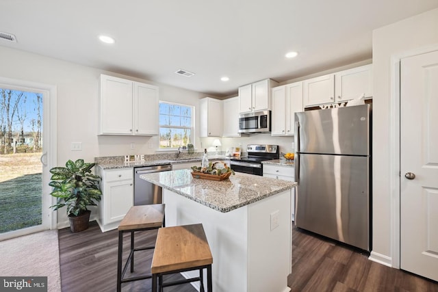 kitchen featuring stainless steel appliances, a kitchen breakfast bar, a center island, light stone countertops, and white cabinets